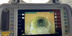 A CCTV drain survey monitor displays a live inspection feed inside a pipe, used to locate a collapsed drain pipe.